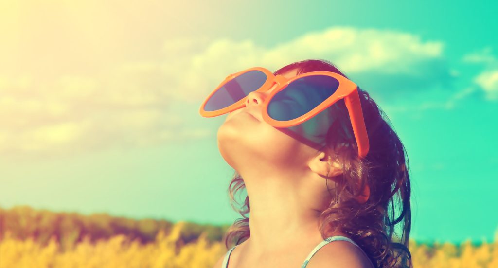 Happy little girl with big sunglasses looking at the sun in the wheat field in summer